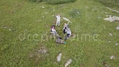 四名游客坐在高高的岩石山脚下的一个绿色的大空地上拍摄一<strong>段视频</strong>，无人机飞离t